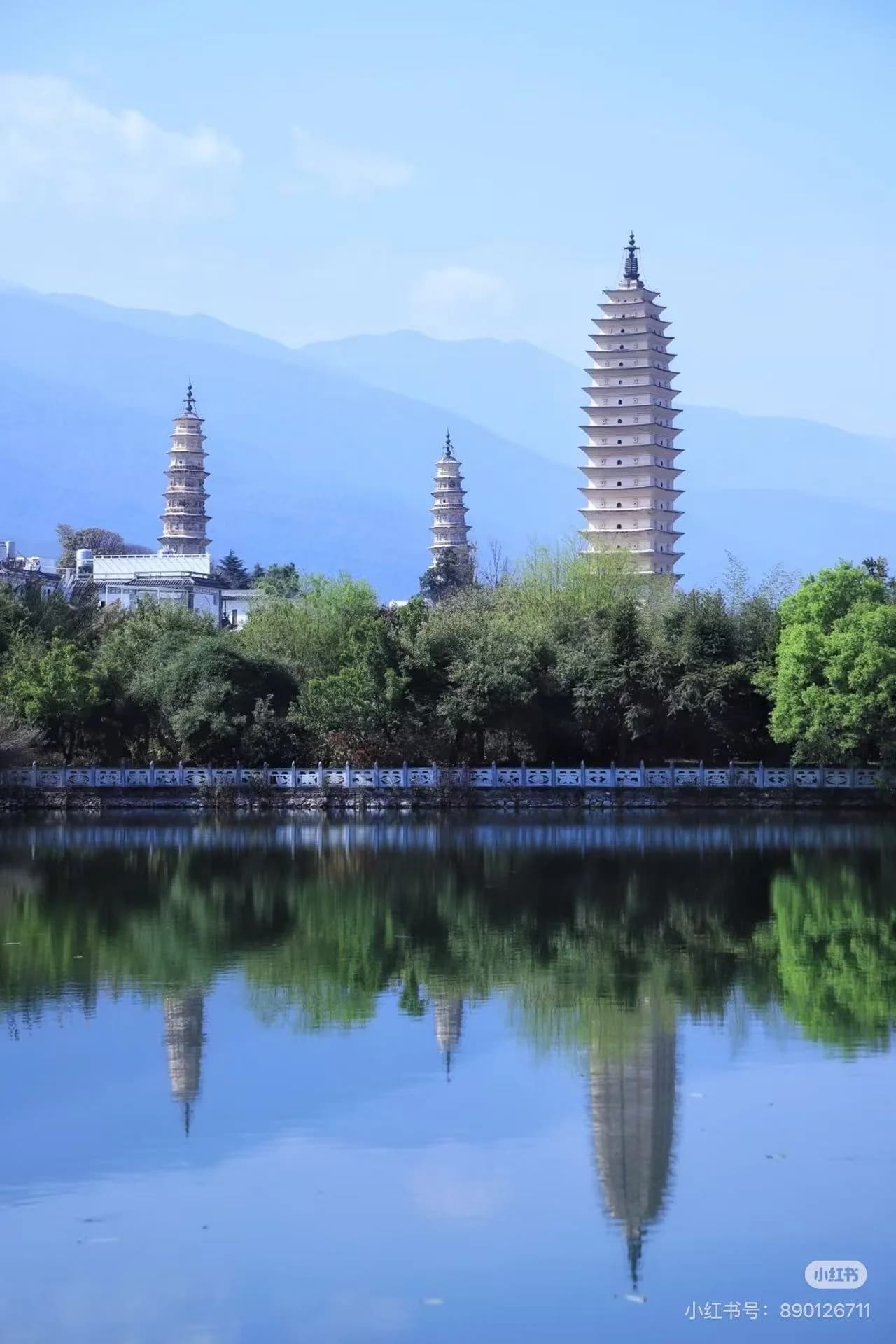 Three white pagodas stand before Cangshan Mountain, reflected in still water, with the tallest pagoda reaching toward the sky