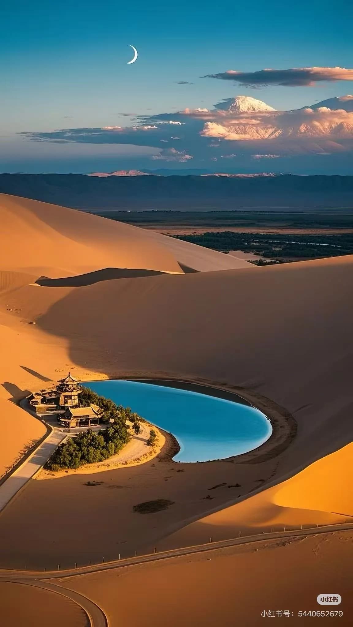 A camel train moving along the ridge of Mingsha Mountain's golden dunes at dusk, with Crescent Moon Spring visible in the valley below