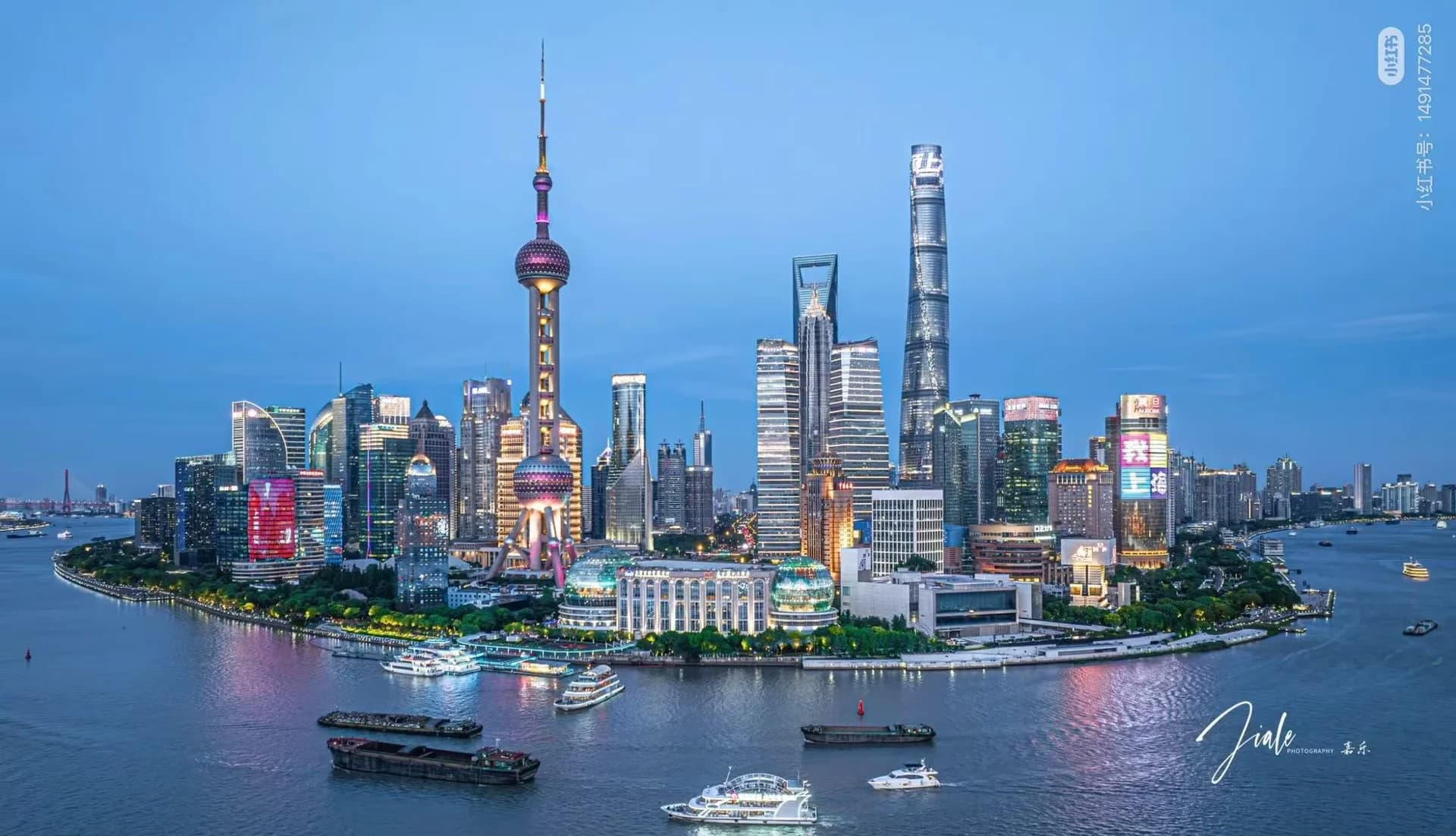 Wide panoramic view of the Pudong skyline at dusk, including the Oriental Pearl Tower and the Shanghai Tower across the Huangpu River.