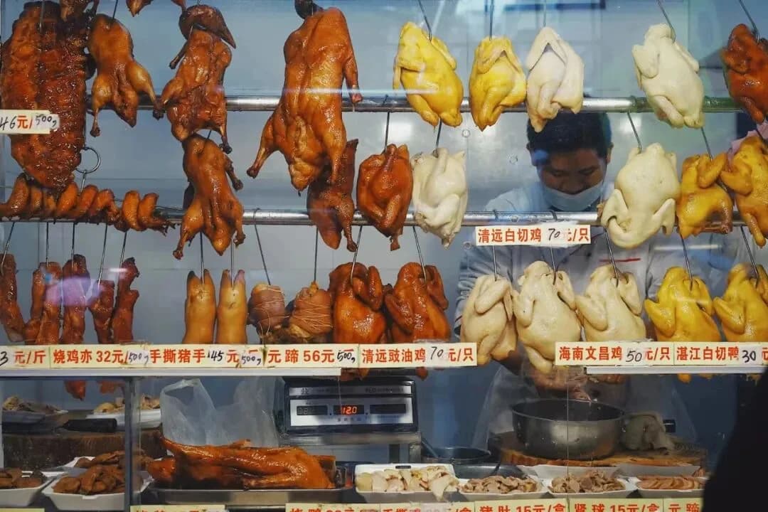 An intercity train departs a station, with modern Guangdong city buildings and lively street life in the foreground.