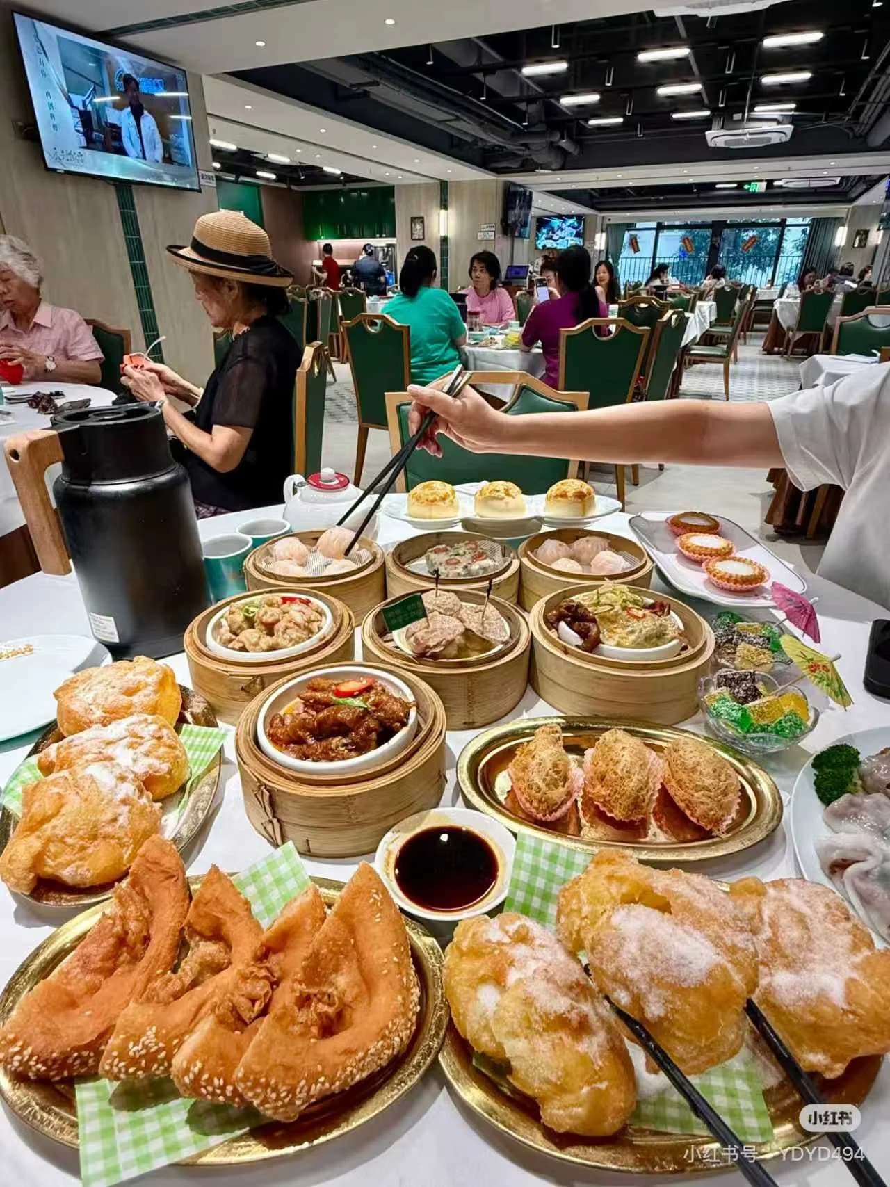 A variety of Cantonese dim sum baskets including har gow, chicken feet, and spare ribs spread across a table in a busy Guangzhou tea house.